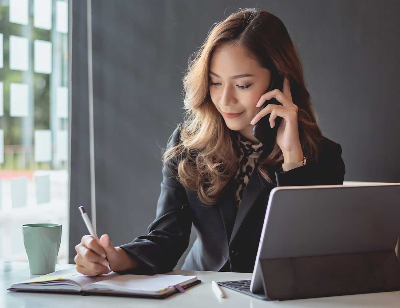 Women on phone call writing notes.