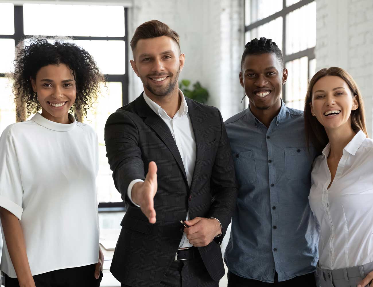 Four people smiling, one with hand outstretched to shake.